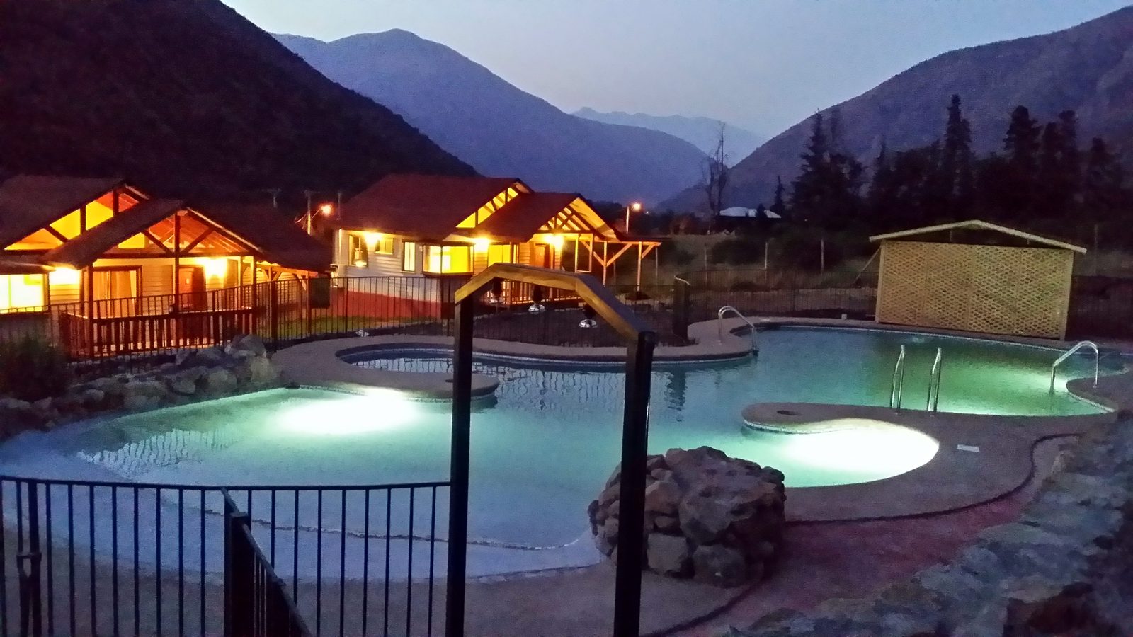 Piscina orgánica iluminada al atardecer junto a cabañas